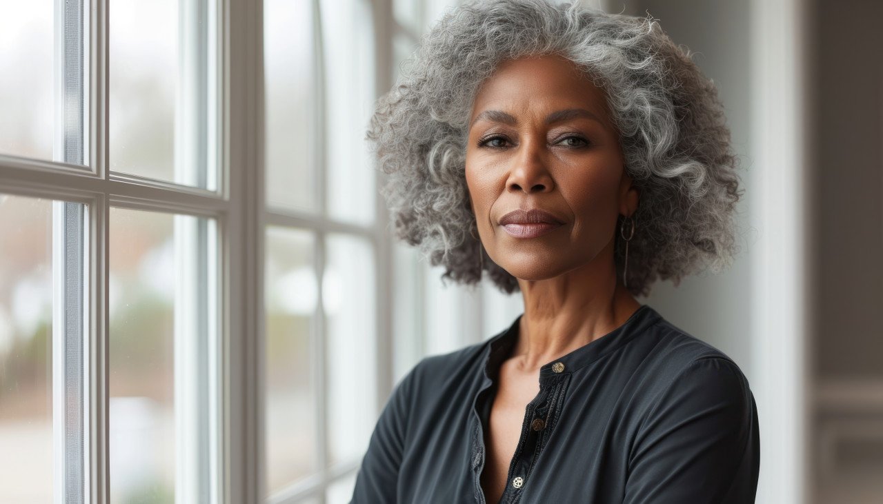Confident beautiful senior woman of african descent standing near indoor window