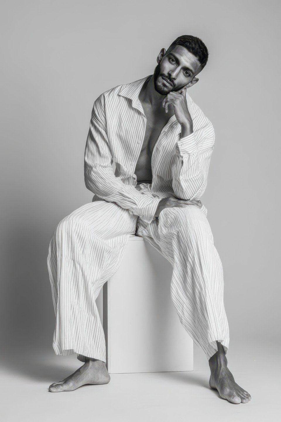 Seated male model in white shirt rests hand on knee