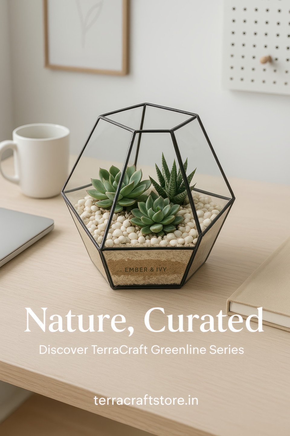 Glass terrarium with succulents and pebbles on wooden desk beside mug